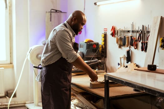 Craftsperson at workbench selecting high quality wood materials for commissioned project. African american woodworking professional doing quality assurance on timber piece