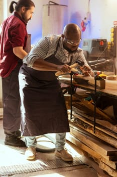 African american manufacturer carving intricate designs into wood using chisel and hammer, wearing safety glasses. Artisan in woodworking workshop shaping wooden pieces using protective equipment