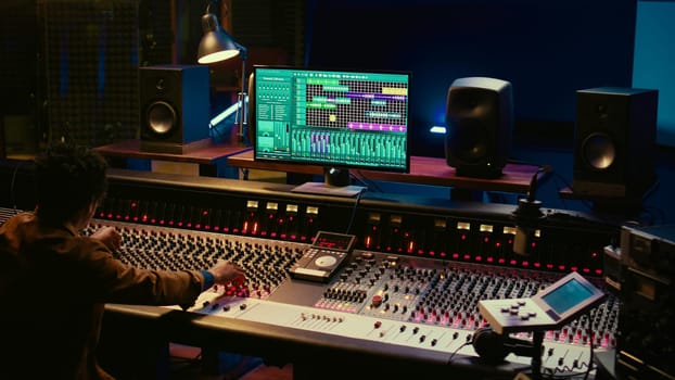 African american audio expert adding sound effects on tracks in post production, operating mixing console and pushing sliders. Producer creating music for his new album, audio mixer. Camera B.