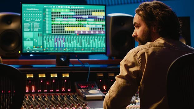 Team of artist and technician editing audio after recording session in control room, mixing and mastering tracks on console in control room. Pressing buttons and pushing sliders. Camera A.