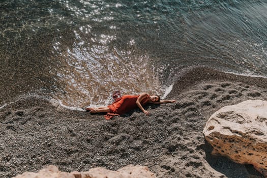 Woman red dress sea. Female dancer in a long red dress posing on a beach with rocks on sunny day.