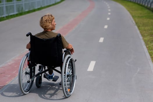 Rear view of an elderly woman in a wheelchair riding on a bike path