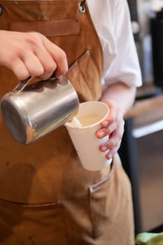 Barista girl pours draws milk over a coffee - making latte art for cappuccino. High quality 4k footage