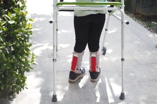 child with walking frame and knee orthosis outdoor .