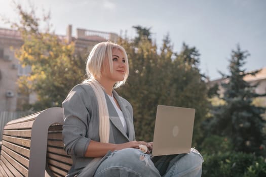 A woman is sitting on a bench with a laptop in front of her. She is smiling and she is enjoying her time