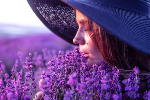 Close up portrait of young beautiful woman in a white dress and a hat is walking in the lavender field and smelling lavender bouquet.