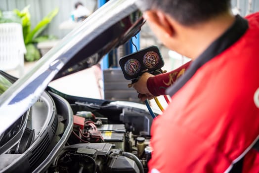 Bangkok, Thailand - May 4, 2023 : Unidentified car mechanic or serviceman refilling air condition and checking a air compressor for fix and repair problem at car garage or repair shop