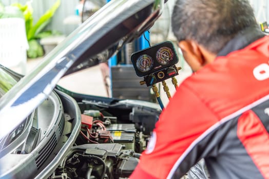 Bangkok, Thailand - May 4, 2023 : Unidentified car mechanic or serviceman refilling air condition and checking a air compressor for fix and repair problem at car garage or repair shop