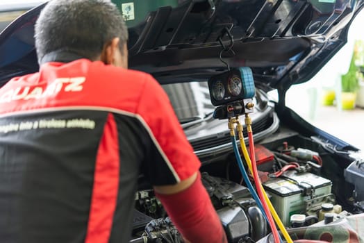 Bangkok, Thailand - May 4, 2023 : Unidentified car mechanic or serviceman refilling air condition and checking a air compressor for fix and repair problem at car garage or repair shop