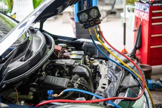 Bangkok, Thailand - May 4, 2023 : Unidentified car mechanic or serviceman refilling air condition and checking a air compressor for fix and repair problem at car garage or repair shop