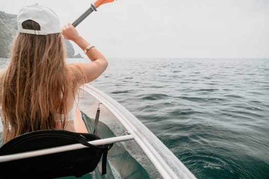 Woman in kayak back view. Happy young woman with long hair floating in transparent kayak on the crystal clear sea. Summer holiday vacation and cheerful female people having fun on the boat.