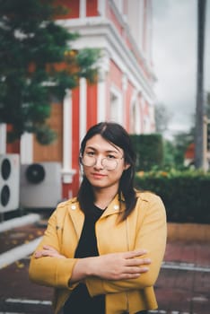 Beautiful asian woman (LGBTQ) natural makeup wear fashion yellow leather clothes with glasses posing at old town and vintage building outdoor fashion style