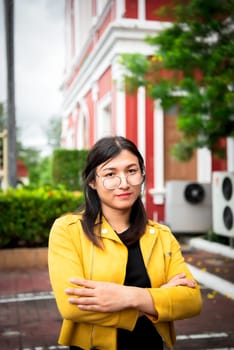 Beautiful asian woman (LGBTQ) natural makeup wear fashion yellow leather clothes with glasses posing at old town and vintage building outdoor fashion style