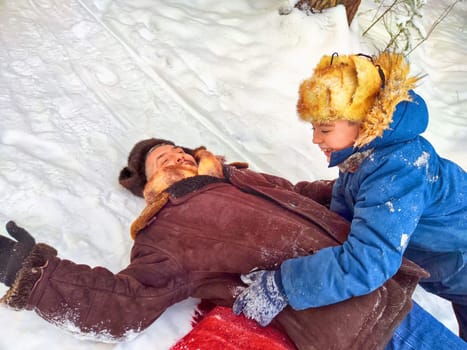 Father and son hugging, having fun, walking in snow nature. Photo shoot in stylized clothes of the USSR. Hat with earflaps. Happy dad and teenager child playing in winter park, forest in holidays