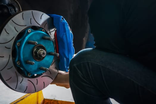 Car mechanic or serviceman disassembly and checking a disc brake and asbestos brake pads for fix and repair problem at car garage or repair shop