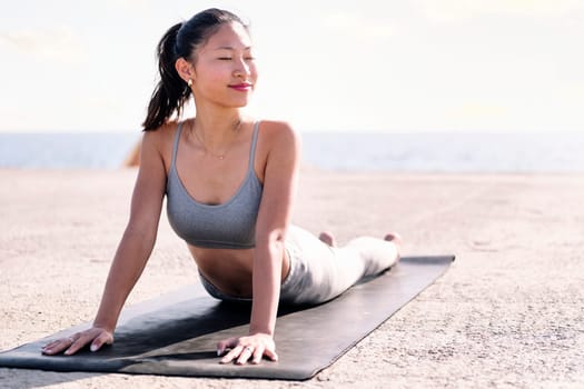 young asian woman in sportswear doing yoga by the sea, concept of mental relaxation and healthy lifestyle, copy space for text