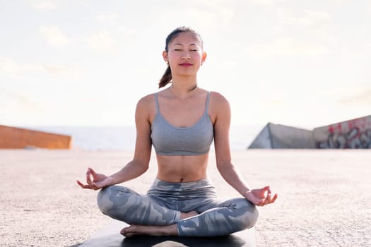 young asian woman doing meditation by the sea sitting on a yoga mat, concept of mental relaxation and healthy lifestyle