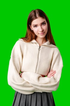 A young woman stands confidently against a vivid green background, dressed in a casual yet fashionable white cropped hoodie and a gray pleated skirt. Her expression is serene with a hint of contemplation, and her body language exudes a relaxed poise.