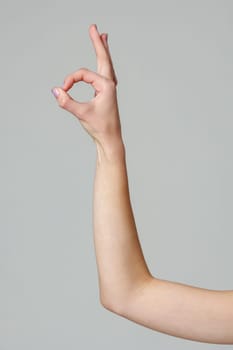 Female hand showing OK sign on gray background close up