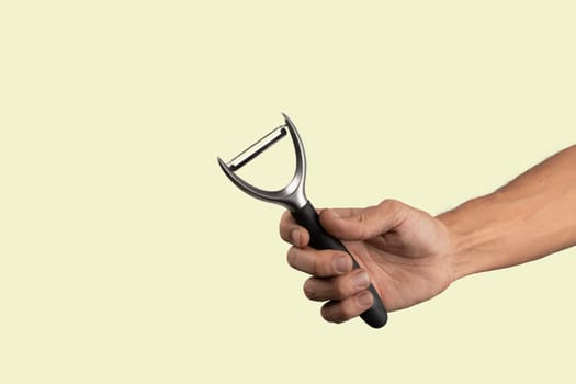 Black male hand holding a potato peeler isolated on green background. High quality photo