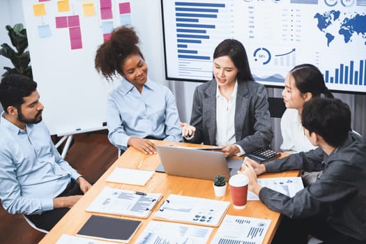 Multiracial analyst team use BI dashboard data to analyze financial report on meeting table. Group of diverse business people utilize data analysis by FIntech for success business marketing. Concord