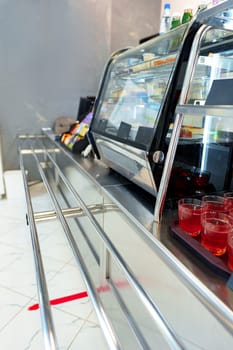 A cafeteria counter is seen with no customers, featuring a snack display, beverage coolers, and prepared drinks on the counter, likely captured during a quiet period or before opening hours.