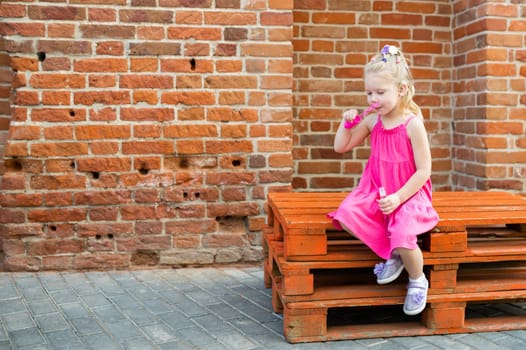 Child girl with hearing aid cochlear implant in pink dress having fun on summer street. Aid for the treatment of deafness and hearing loss in humans. Copy space.