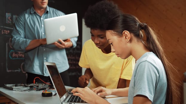 Group of diverse student working together to write program. Multicultural children coding or programing program while teacher holding laptop and looking at smart learner at STEM class. Edification.