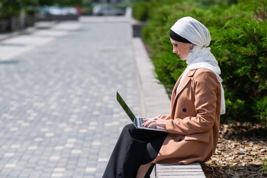 Portrait of young woman in hijab using laptop outdoors