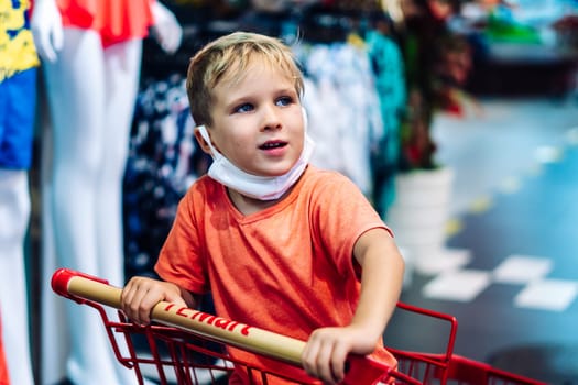 Boy sitting in shopping cart clothing store hypermarket, interested curious emotion, happy childhood.