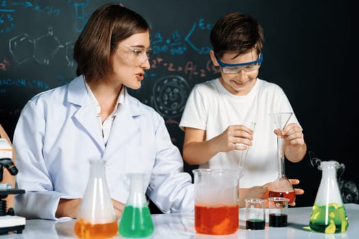 Teacher in support and watch student in laboratory they wear safety glasses, stand and experiment about science of chemistry in STEM class. Student funny do experiment with liquid in tube. Erudition.