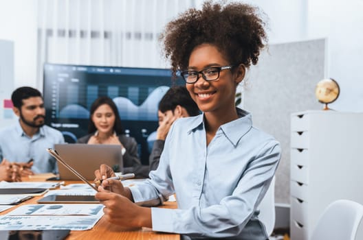 Happy young african businesswoman wearing glasses portrait with group of office worker on meeting with screen display business dashboard in background. Confident office lady at team meeting. Concord