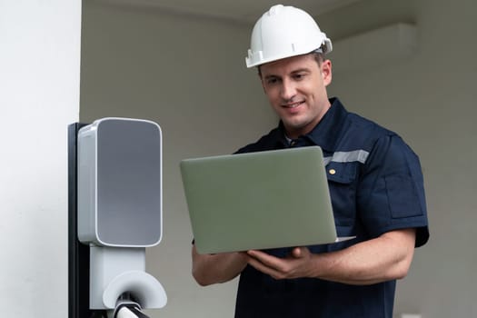 Qualified technician working on home EV charging station installation, making troubleshooting and configuration setup on charging system with laptop for EV at home. Synchronos