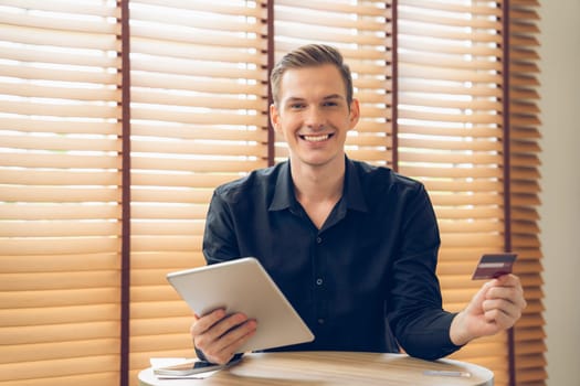 Young man using tablet with credit card for internet banking, online shopping E commerce by online payment gateway at home office. Modern and convenience online purchasing with debit card. Unveiling