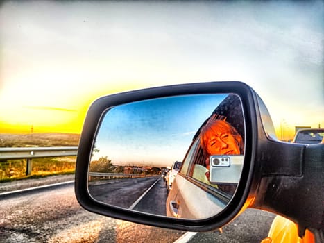 The side mirror of the car and the sun with bright rays behind it and the track on trip in nature