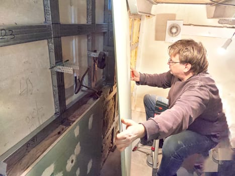 Professional Installs Drywall During Home Renovation. A skilled worker measures and secures drywall in a home under renovation