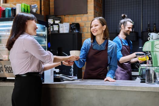 Woman customer of coffee shop near counter with cup of coffee talking to restaurant workers owners. Workplace at bar, colleagues, partners in food service, work, entrepreneurship, small business