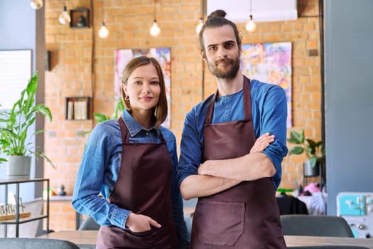 Small business team portrait of confident successful colleagues partners young man woman in aprons posing looking at camera at workplace in restaurant coffee shop cafeteria. Partnership teamwork work