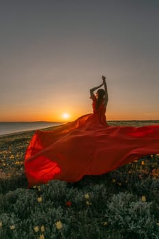 A woman in a red dress is standing in a field with the sun setting behind her. She is reaching up with her arms outstretched, as if she is trying to catch the sun. The scene is serene and peaceful