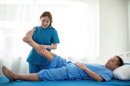 Physical therapist Asian woman, doing leg physiotherapy for elderly man to treat osteoarthritis and nerve pain in the leg to nursing at home and health care concept.