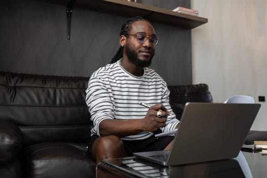 African American man working with document and laptop at home on couch. work from home concept.