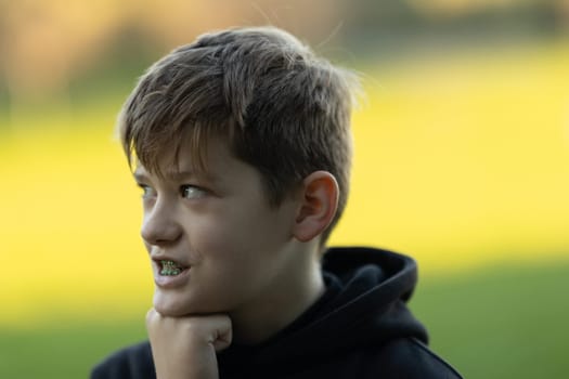 A boy with braces is looking at the camera. He is wearing a black hoodie and has a black and white striped shirt on