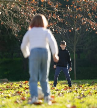 A boy and a girl are playing in a park. The boy is wearing a black hoodie and the girl is wearing a white shirt