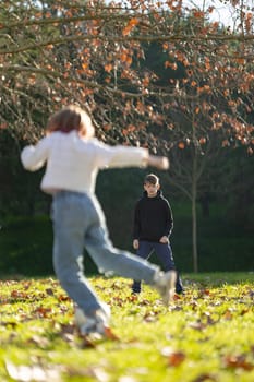 Two children playing in a park. One is wearing a white shirt and jeans, while the other is wearing a black hoodie
