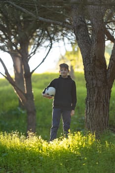 A boy is standing in a field with a soccer ball in his hand. Concept of playfulness and enjoyment, as the boy is likely preparing to play a game of soccer. The lush green grass