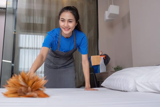 A beautiful young housekeeper does housework wearing orange rubber and uses a duster to clean up the items in the room..