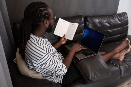 Young African American businessman spends his weekend working from home using his laptop in the living room..