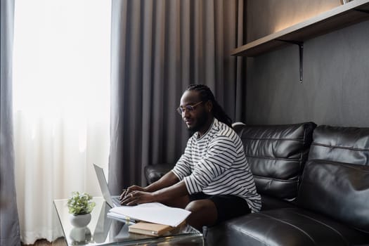 African American man working with document and laptop at home on couch. work from home concept.