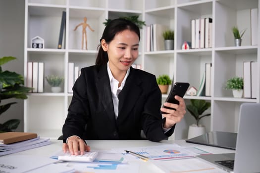 Asian female accountant Use a calculator to calculate business numbers on a white wooden table in the office..