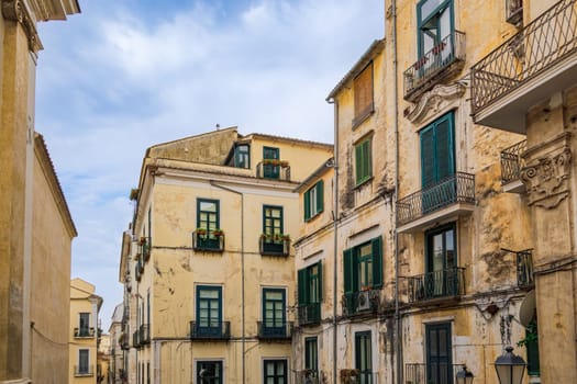 Salerno, Italy historic buildings with iron balconies and wooden window shutters under a sky with clouds.